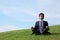 Businessman meditates sitting on meadow