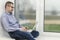 Businessman, an office worker in a blue shirt, sits on a windowsill with a laptop. Communicates online and works. Online