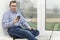 Businessman, an office worker in a blue shirt, sits on a windowsill with a mobile phone. Communicates by phone. Online