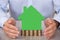 Businessman protecting green model house on stacked coins