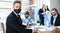 Businessman in protective mask sitting in the office with his colleagues on a background