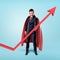 A businessman in a red flowing cape trying to keep the upward looking red arrow with his hand.