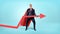 A businessman in a red flowing cape trying to lift a large red arrow upwards on blue background.