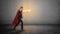 A businessman in a red superhero cape and a flaming hand throwing punches at an invisible enemy on concrete background.