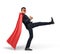 A businessman in a red superhero cape kicking an invisible object on white background.