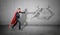 A businessman in a red superhero cape throwing punches at a wall drawing of an UFO striking at him.