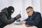 businessman and robbers are sitting at a table. A racketeer in a black balaclava forces to sign a contract. The concept