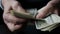 A businessman\'s hands counting hundred dollar bills at a table