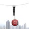 Businessman shackled by debt ball hanging on rope with cityscape