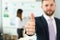 Businessman showing thumb up sign of success over blurred team of business people