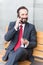 Businessman sitting on bench using his cell phone. Smiling bearded businessman sitting on bench and talking on the phone