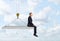 Businessman sitting on concrete slab suspended from construction crane hook.