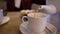 Businessman sitting at a table in cafe pour tea into a white mug. Man hands with white teapot in the restaurant. A man