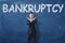 Businessman standing with his hands like cross sign and word `Bankruptcy` written on blackboard behind him