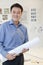 Businessman standing with rolled up blueprint in the office, portrait