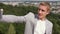 Businessman stands on a hill and makes selfie on city background