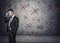 Businessman stands pondering on the concrete background with depicted ideas that crossed by red