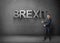 Businessman stands showing big 3d \'brexit\' word by both hands on concrete background