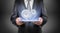 A businessman in a suit holds a glowing tablet with two interlocked metal spur gears hovering above it.