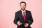 Businessman in suit and red tie holds smartphone on pink background. Bearded officer welcomes with you.