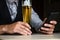 Businessman on suits sits on a bar with a glass of beer and with work phone.  Working on home