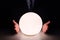 Businessman using glowing crystal ball to predict future at table in darkness, closeup. Fortune telling