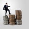 Businessman walking on coins stack on gray