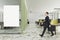 Businessman walking in office interior with blank poster