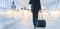 Businessman walking and wheeling a trolley suitcase at the lobby, talking on a mobile phone. Business travel concept.