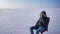 Businessman in warm coat and hood sitting in snow desert talking happily on cellphone and smiling.