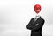 A businessman on white background stands with crossed hands and a red angry face balloon instead of his head.