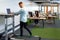 Businessman working on laptop while exercising on treadmill in a modern office