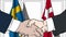 Businessmen or politicians shake hands against flags of Sweden and Denmark. Official meeting or cooperation related