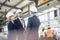 Businessmen shaking hands with workers working in background at metal industry