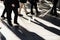 Businessmen walking fast on city sidewalk silhouetted in bright sunlight, one man stands out wearing light pants, different