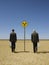 Businessmen Walking Past Road Sign In Desert