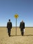 Businessmen Walking Past Road Sign In Desert