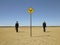 Businessmen Walking Past Road Sign In Desert
