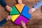 Businesspeople Holding Multicolored Pie Chart Over Desk