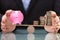 Businessperson Protecting Piggy Bank And Stacked Coins On Seesaw