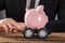 Businessperson Pushing Piggy Bank On Wheels