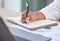 Businessperson writing in a notebook working in an office at work. Closeup of a business professional holding a pen and