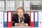 Businesswoman Behind Binders Sitting At Desk