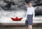 Businesswoman with briefcase and red paper boat in sea