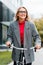Businesswoman in coat and glasses smiling and riding bike