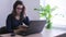 Businesswoman in eyeglasses flipping magazine sitting in front of laptop computer at work