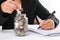 Businesswoman holds a coin in her hand with glass jar with coins at workplace. Financial saving and investment concepts