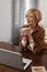 Businesswoman. Mature Woman In Brown Jacket And Eyeglasses Drinks From Cup. Laptop At The Desk.