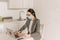 Businesswoman in medical mask typing on laptop with coronavirus sticker in kitchen