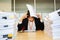 Businesswoman resting hand on head eyes close with pile of paperwork.